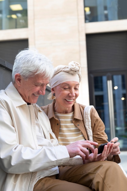 Coppia di anziani sorridente che utilizza smartphone insieme all'aperto