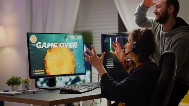 Coppia di giocatori stressati che perdono il videogioco sparatutto spaziale giocando su un potente computer RGB durante lo streaming della competizione online. Pro cyber donna con auricolare che si esibisce da casa durante il torneo virtuale