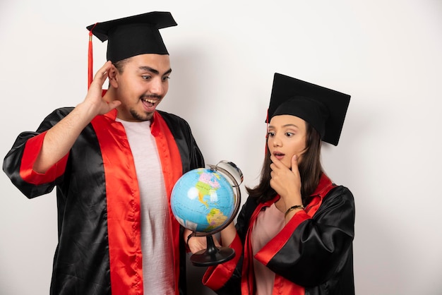 Coppia di studenti felici in abito guardando il globo su bianco.