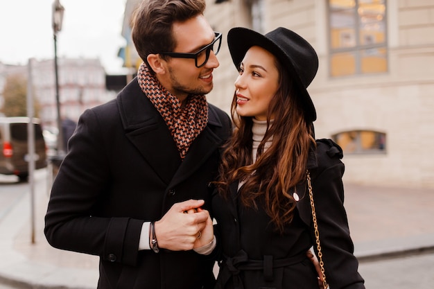 Coppia elegante alla moda all'aperto innamorata imbarazzante e guardandosi l'un l'altro con adorazione. Donna castana in cappello di lana con il suo fidanzato in sciarpa e cappotto.