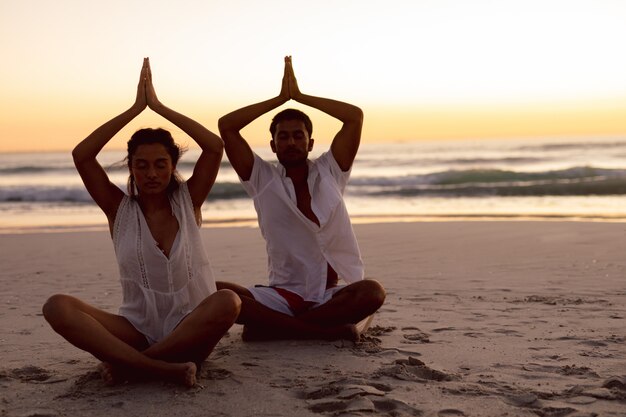 Coppia eseguendo yoga insieme sulla spiaggia