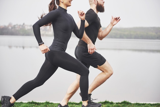 Coppia fare jogging e correre all'aperto nel parco vicino all'acqua. Giovane uomo e donna barbuti che si esercitano insieme nella mattina