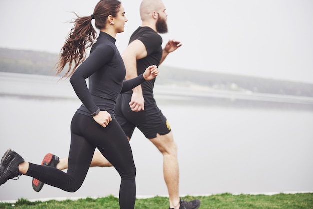 Coppia fare jogging e correre all'aperto nel parco vicino all'acqua. Giovane uomo e donna barbuti che si esercitano insieme nella mattina