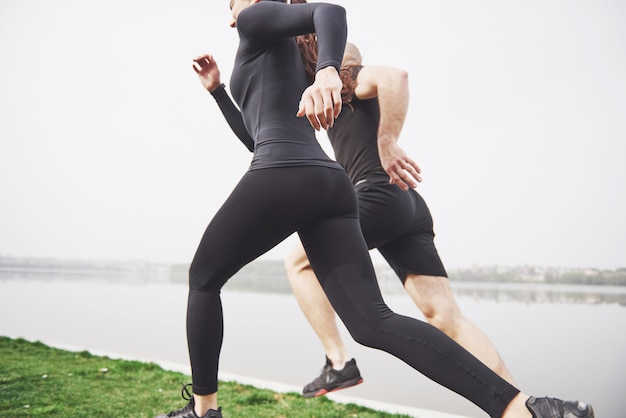 Coppia fare jogging e correre all'aperto nel parco vicino all'acqua. Giovane uomo e donna barbuti che si esercitano insieme nella mattina