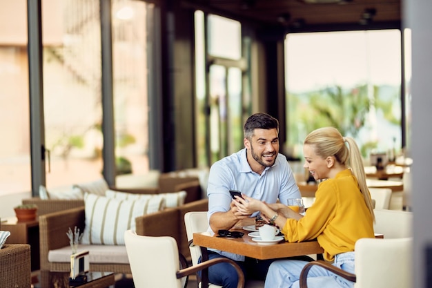 Coppia felice che comunica durante l'utilizzo del telefono cellulare in un bar