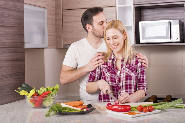 Coppia felice che prepara un'insalata fresca con verdure sul bancone della cucina