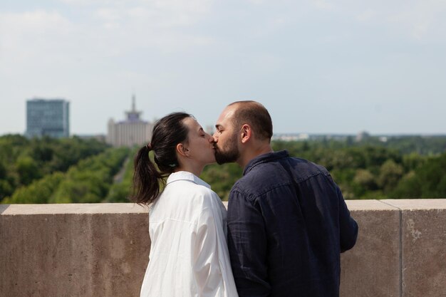 Coppia felice sposata che si bacia sul tetto della torre per celebrare l'anniversario della relazione in piedi al punto di osservazione godendo della splendida vista sulla città metropolitana. Paesaggio con edifici urbani