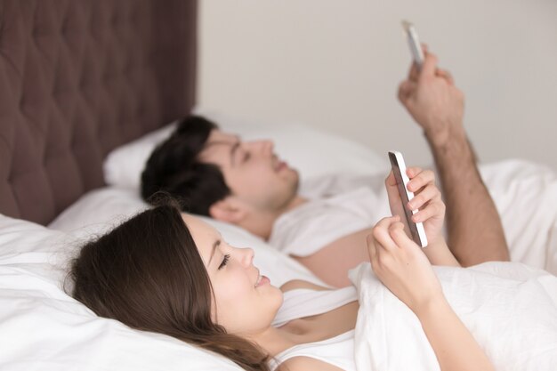 Coppia felice tutti con il proprio smartphone sdraiato sul letto