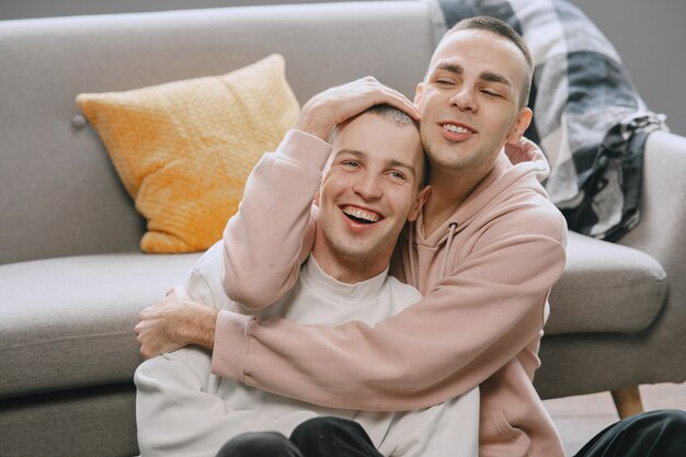 Coppia gay nel loro appartamento. Abbracciarsi e sedersi sul pavimento. omosessuale.