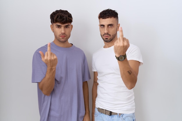 Coppia gay omosessuale in piedi su sfondo bianco che mostra il dito medio, maleducato e maleducato vaffanculo espressione