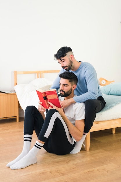 Coppia gay seduto con il suo fidanzato leggendo il libro in camera da letto