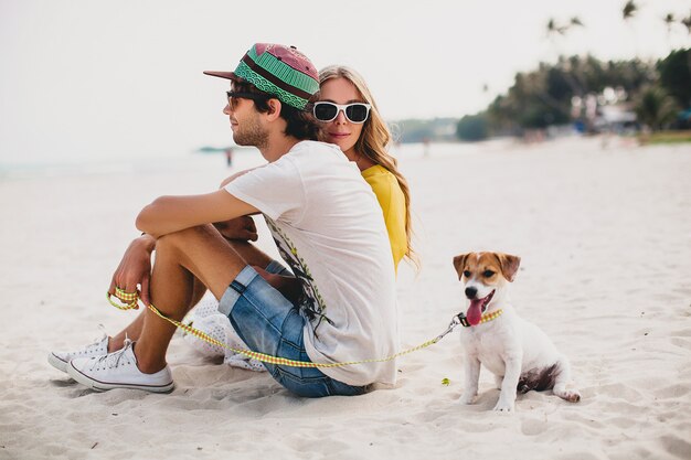 Coppia giovane elegante hipster in amore camminare e giocare con il cane in spiaggia tropicale