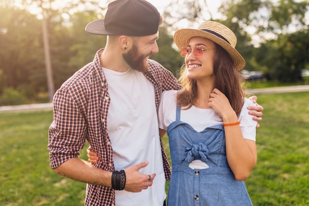 Coppia giovane piuttosto hipster che cammina nel parco, amici che si divertono insieme, romanticismo alla data, stile moda estiva, vestito colorato hipster, uomo e donna che sorridono abbracciando