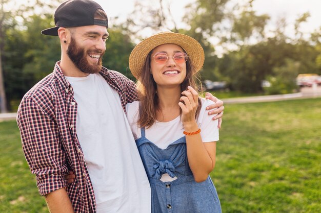 Coppia giovane piuttosto hipster che cammina nel parco, amici che si divertono insieme, romanticismo alla data, stile moda estiva, vestito colorato hipster, uomo e donna che sorridono abbracciando