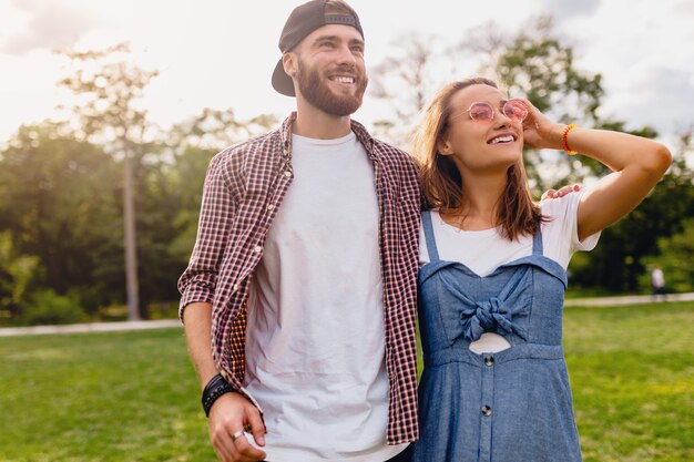 Coppia giovane piuttosto hipster che cammina nel parco, amici che si divertono insieme, romanticismo alla data, stile moda estiva, vestito colorato hipster, uomo e donna che sorridono abbracciando