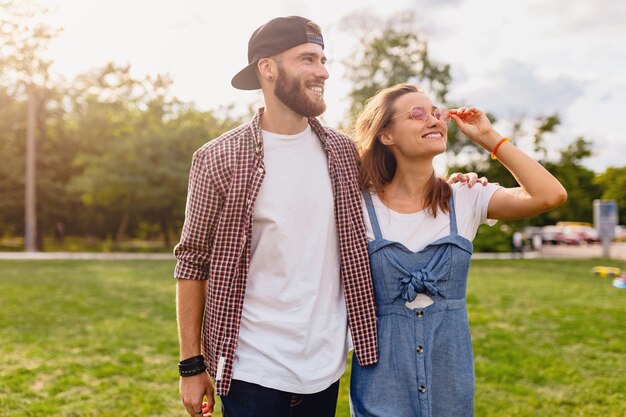 Coppia giovane piuttosto hipster che cammina nel parco, amici che si divertono insieme, romanticismo alla data, stile moda estiva, vestito colorato hipster, uomo e donna che sorridono abbracciando