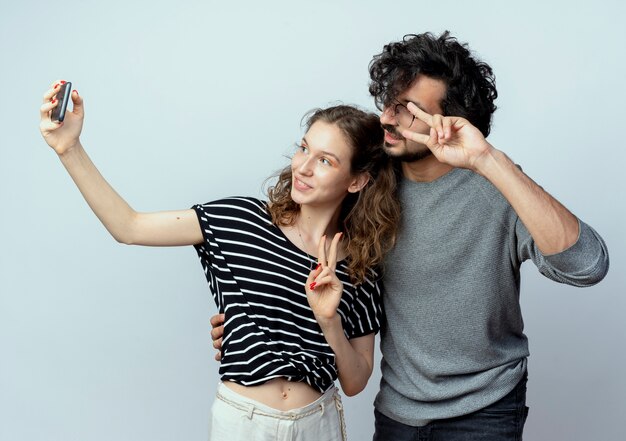 Coppia giovane uomo e donna felice in amore, donna felice di scattare una foto di loro utilizzando lo smartphone in piedi su sfondo bianco
