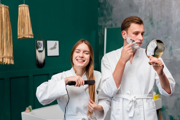 Coppia in accappatoi, rasatura e stiratura dei capelli