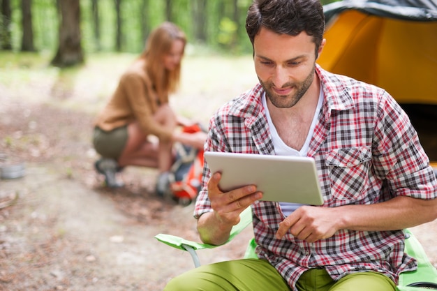 Coppia in campeggio nella foresta. Uomo che utilizza una tavoletta digitale