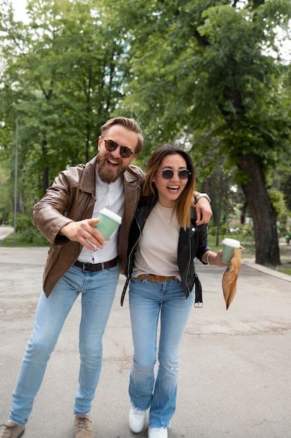 Coppia in giacche di pelle sintetica che beve caffè e snack mentre si cammina all'aperto