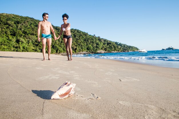 Coppia in spiaggia con conchiglia in primo piano