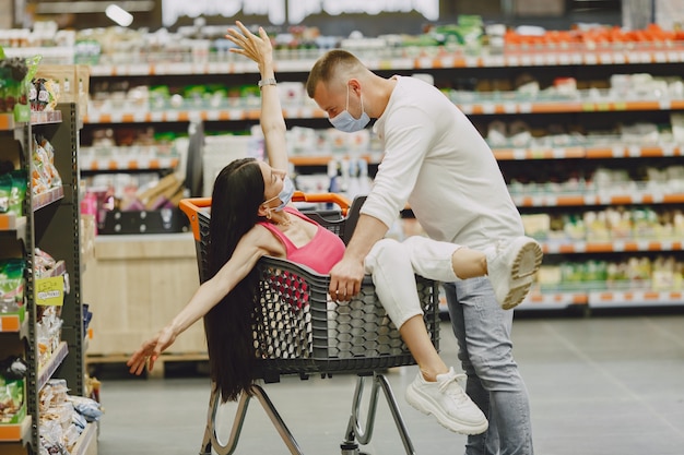 Coppia in un supermercato. Signora in una maschera medica. La gente fa acquisti.