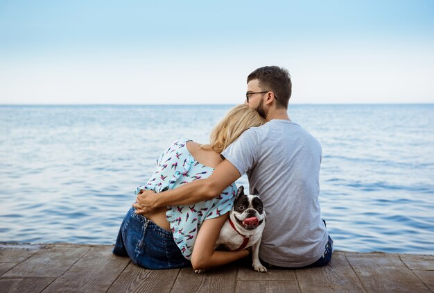 Coppia la seduta con il bulldog francese vicino al mare