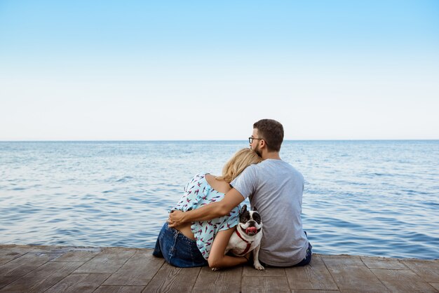 Coppia la seduta con il bulldog francese vicino al mare