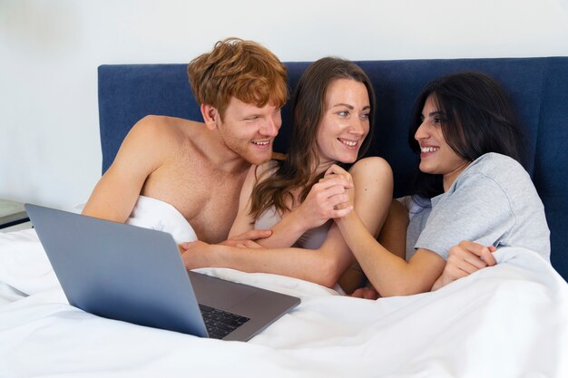 Coppia poliamorosa a casa a letto con il laptop