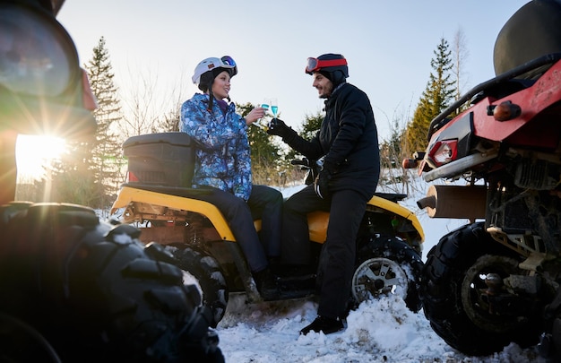 Coppia romantica all'aperto in inverno che celebra con champagne blu seduto su un ATV giallo