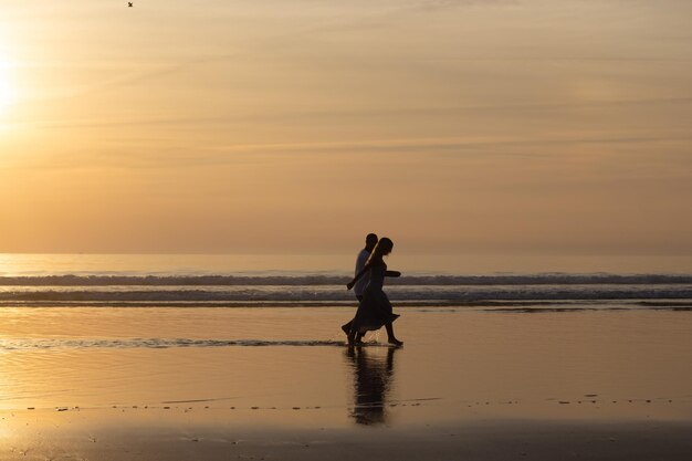 Coppia romantica che cammina sulla spiaggia al tramonto. Uomo e donna in abiti casual che passeggiano lungo l'acqua al tramonto. Amore, famiglia, concetto di natura