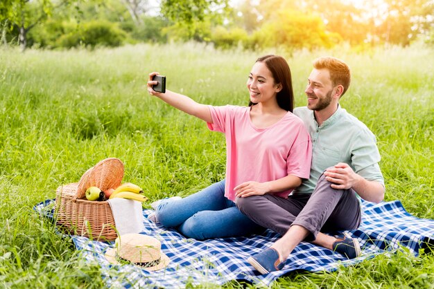 Coppia seduta nel parco e prendendo selfie