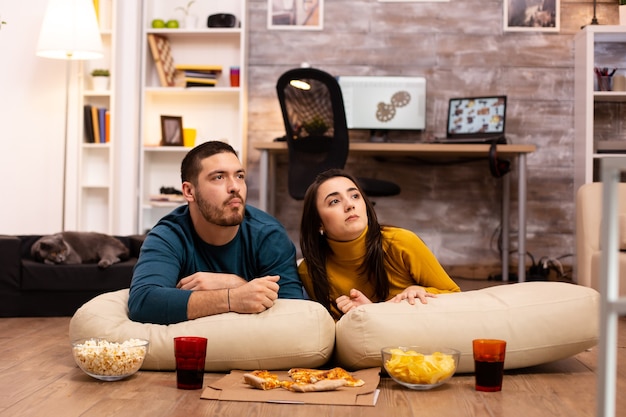 Coppia seduta sul pavimento e guardare la TV nel loro soggiorno.