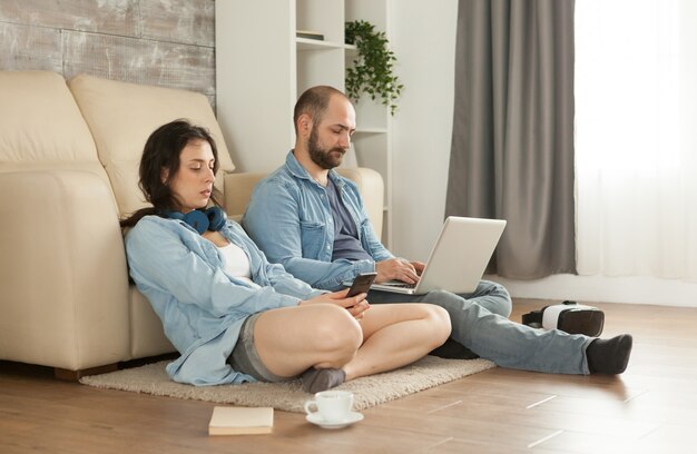 Coppia seduta sul tappeto del soggiorno che naviga su internet
