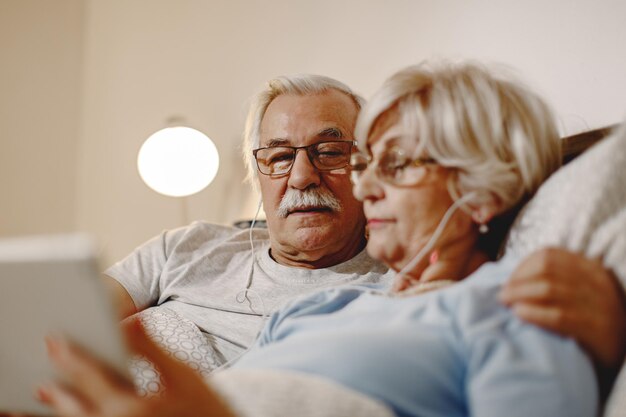 Coppia senior che naviga in Internet su tavoletta digitale mentre si riposa in camera da letto Focus è sull'uomo