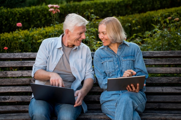 Coppia senior di smiley all'aperto sul banco con laptop e tablet