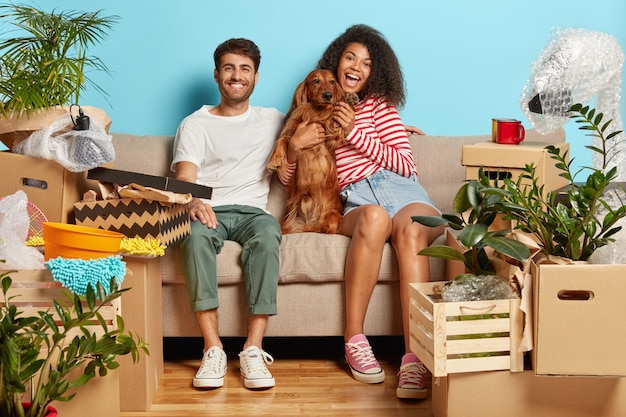 Coppia sposata felice sul divano con il cane circondato da scatole di cartone