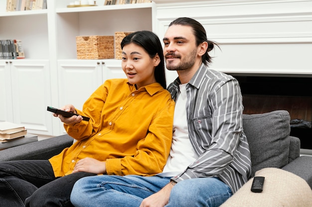 Coppia vista laterale seduta sul divano a guardare la tv