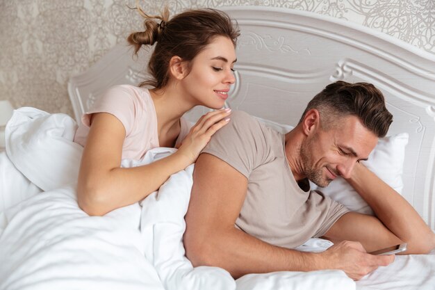 Coppie adorabili sorridenti che si trovano insieme a letto