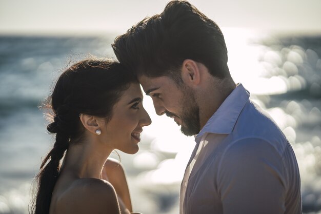 Coppie amorose caucasiche che indossano vestiti bianchi e che abbracciano in spiaggia durante un servizio fotografico di matrimonio