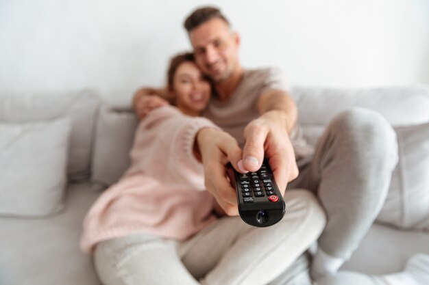 Coppie amorose sorridenti che si siedono insieme sullo strato e che guardano TV. Focus sul telecomando della TV