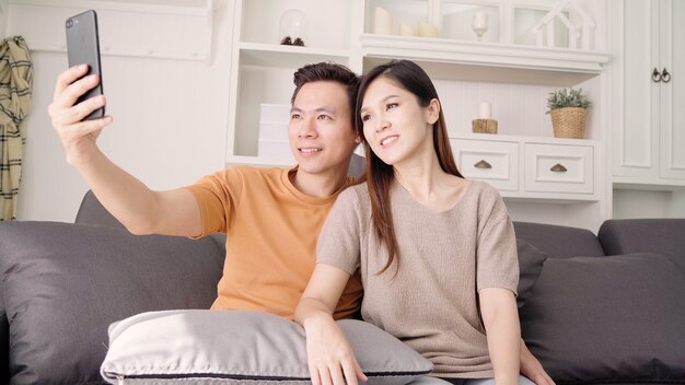 Coppie asiatiche che utilizzano smartphone per selfie in salotto a casa