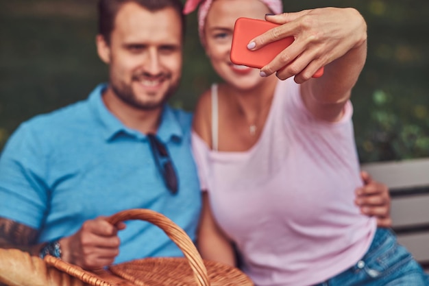 Coppie attraenti sorridenti che prendono selfie ad un picnic in un parco, durante la datazione all'aperto.