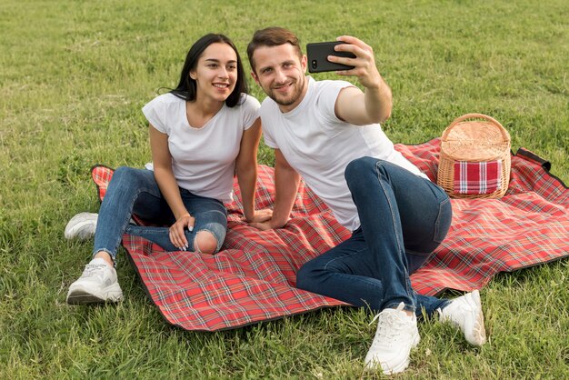 Coppie che prendono un selfie sulla coperta di picnic