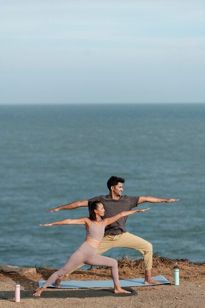 Coppie del colpo pieno che fanno yoga insieme sulla spiaggia