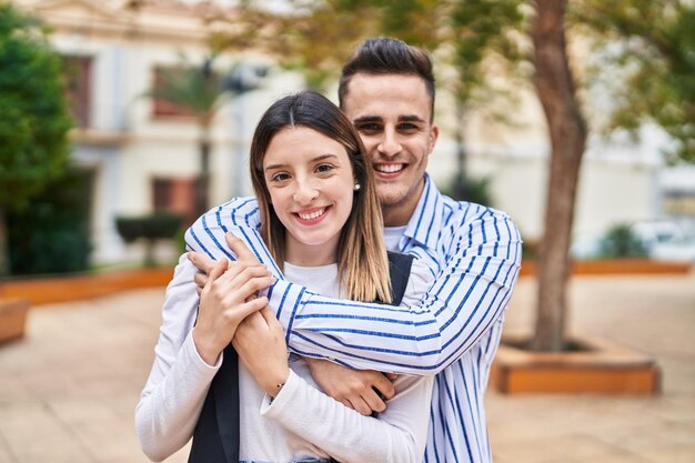 Coppie della donna e dell'uomo che sorridono fiduciosi che si abbracciano al parco