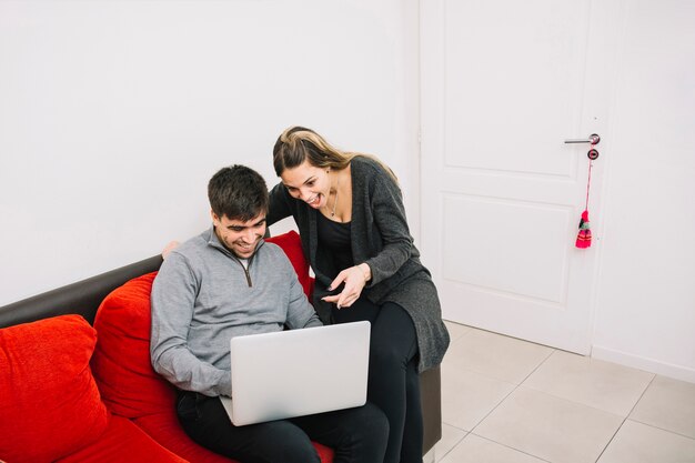 Coppie emozionanti che si siedono sul sofà che esamina lo schermo del computer portatile