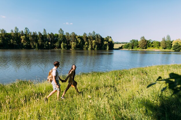 Coppie felici che camminano nell&#39;erba verde vicino al lago idilliaco
