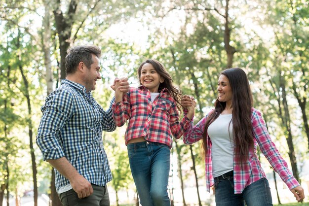 Coppie felici che oscillano la loro figlia fra loro al parco