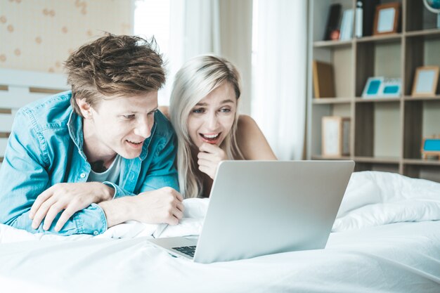 Coppie felici che per mezzo del computer portatile sul letto